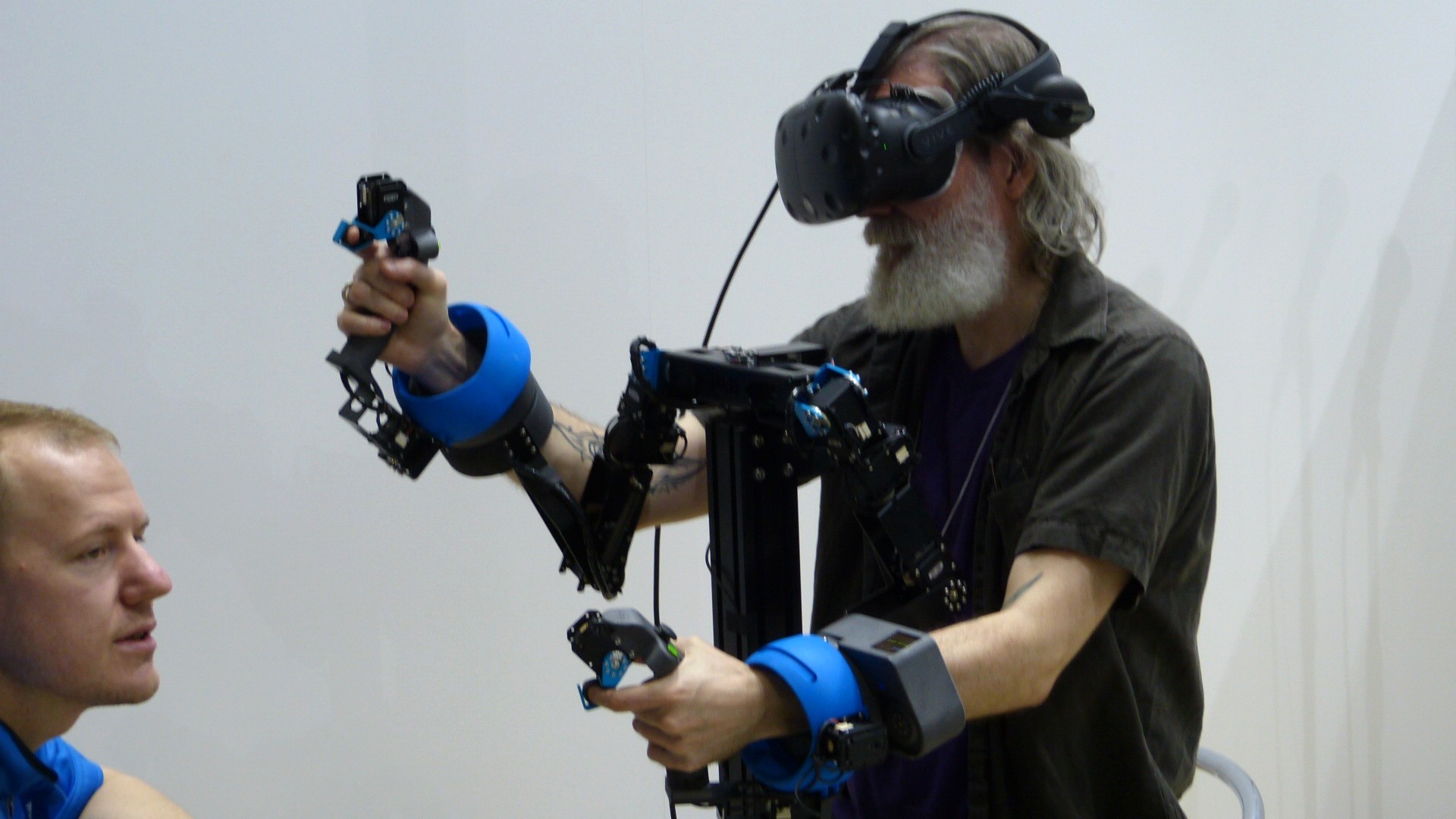 Earl seated with a vr headset on and his hands gripping controllers connected to a frame with arms to limit movement